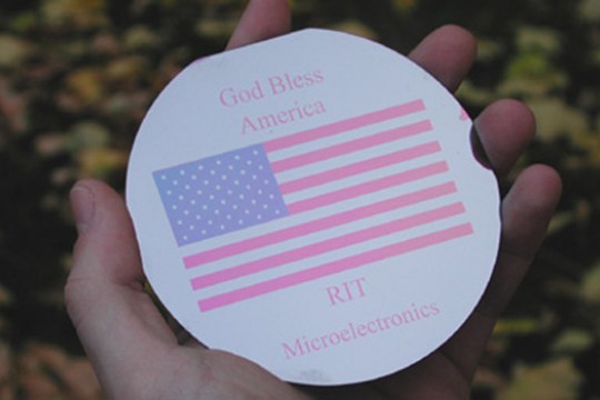 hand holding computer wafer imprinted with American flag and the words God Bless America.