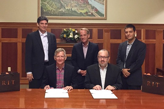 Five men in suits around a table at a ceremony.