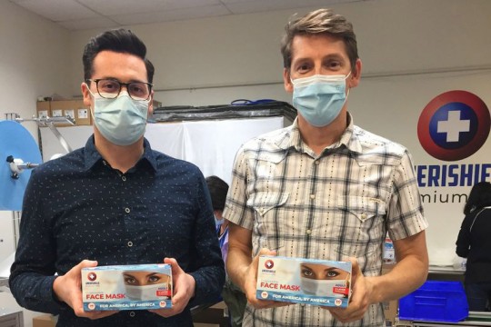 two men wearing disposable fask masks and holding boxes of displosable face masks.