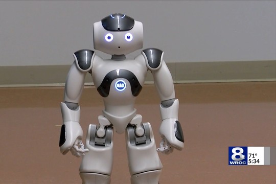 A picture of a small robot with glowing eyes and a logo on the chest that says, "NAO"