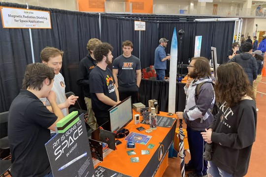 college students around a display table about rockets.