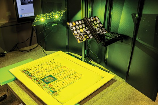 High-resolution scanner digitizing an illuminated manuscript page.