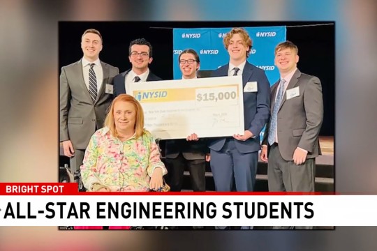 a group of students stand with a large check made out in the amount of fifteen thousand dollars from N Y S I D