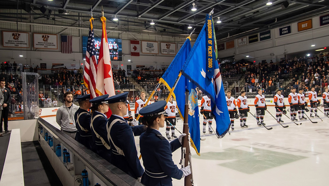 People in dress uniforms, holding flags at a hockey game.