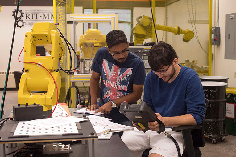 2 students working in a lab with large robot arms.