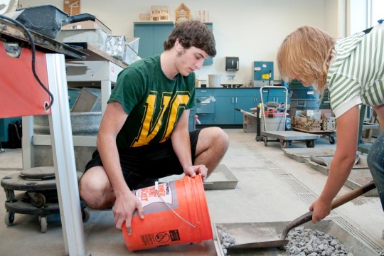 Two students scooping small stones into a 5 gallon bucket.