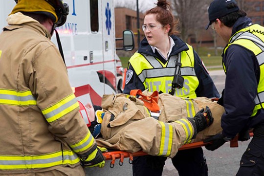 Three people in uniform putting a person on a gurney in the ambulance.