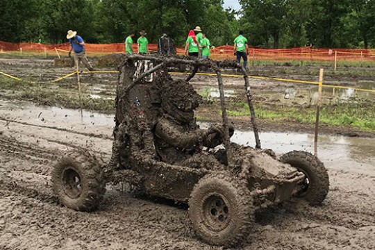 Baja driver in car covered in mud on track.