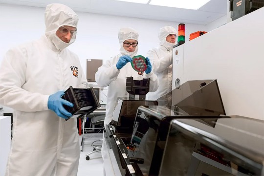 three researchers wearing clean suits handling micro chips.