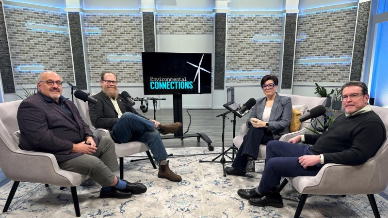 four people sitting in soft chairs in a large radio recording studio.