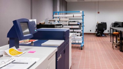 Printer with a rack of rolled paper in the background