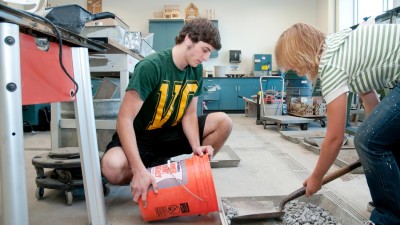 Two students scooping small stones into a 5 gallon bucket.