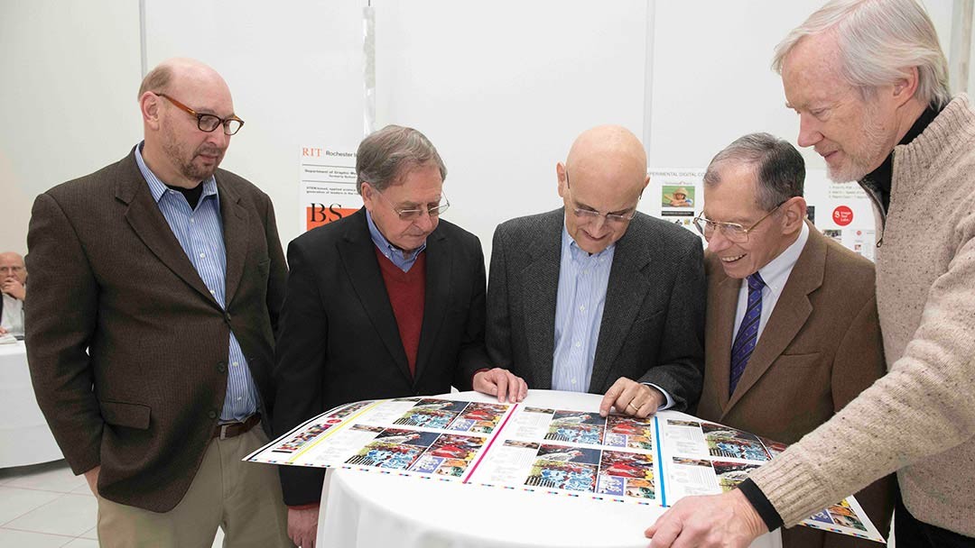 5 men look at a colorful print proof.