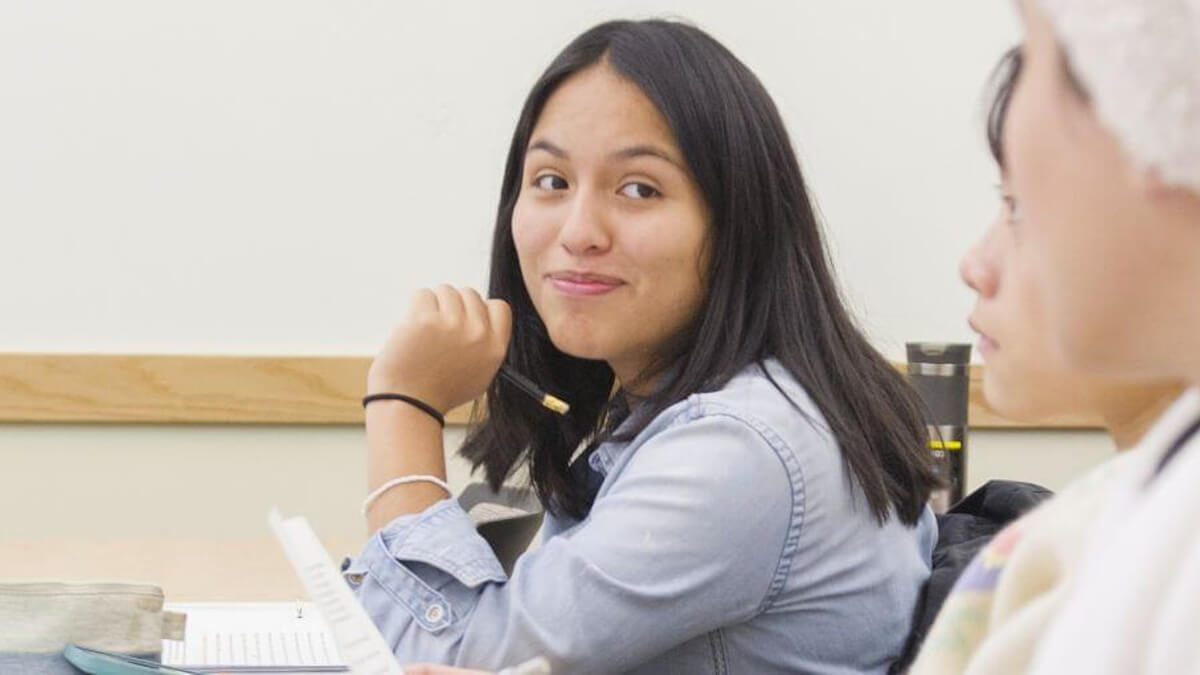 A student smiles at two of her classmates while note taking.