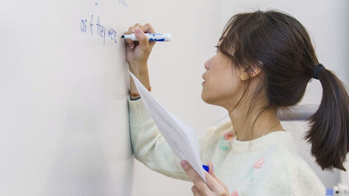 A student writes “as if they were” on a white board.