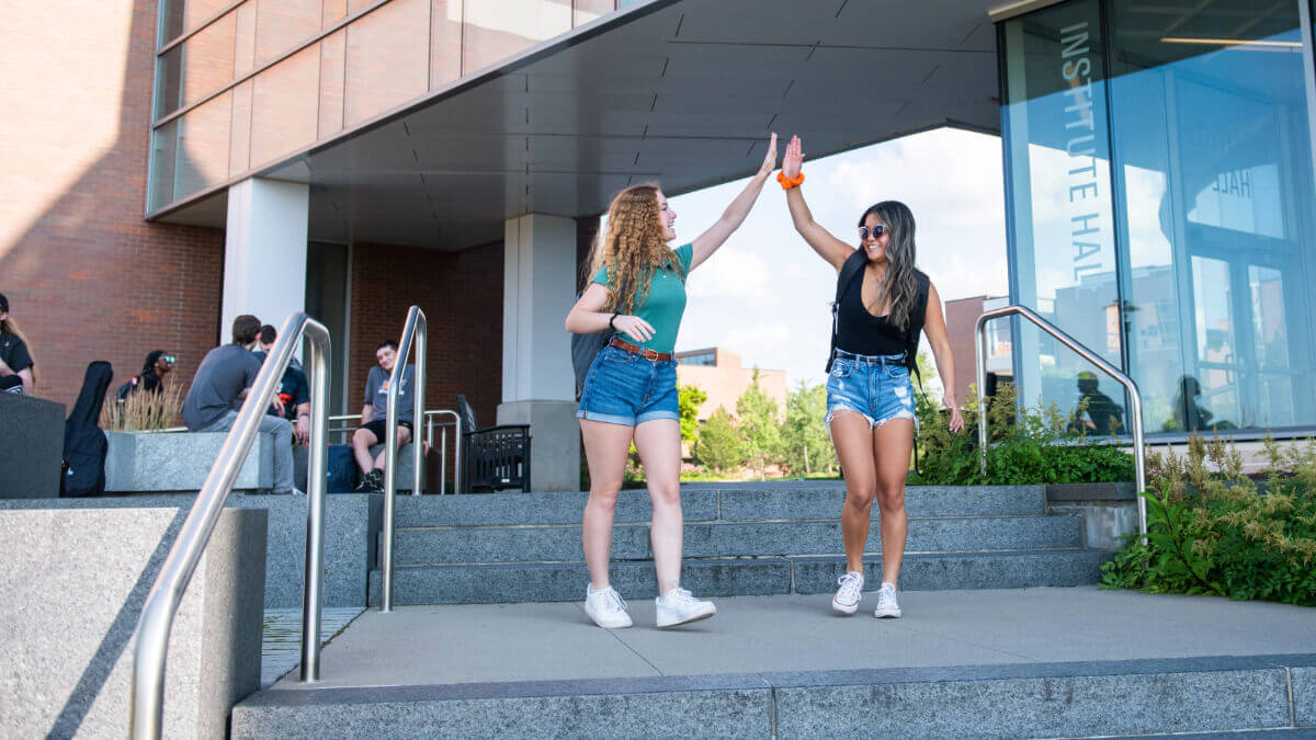 2 students walking while high-fiving each other