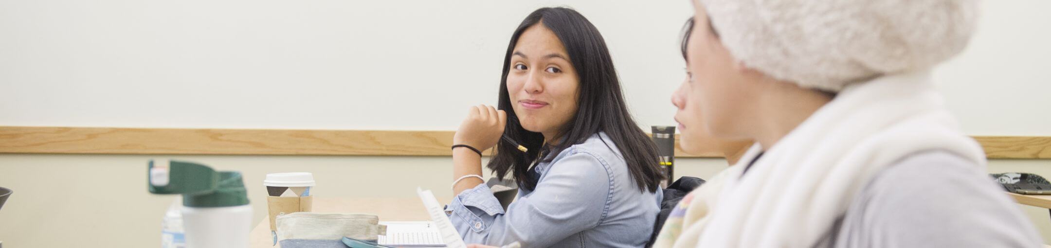 Two students looking sitting at a table, looking at each other.