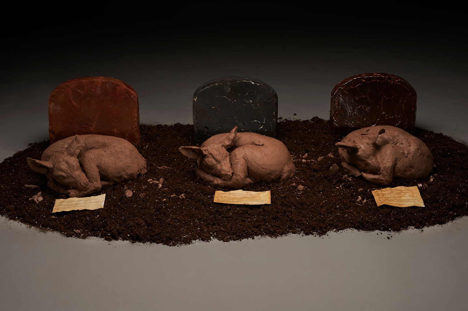 Three ceramic sculptures of pigs laying next to graves.