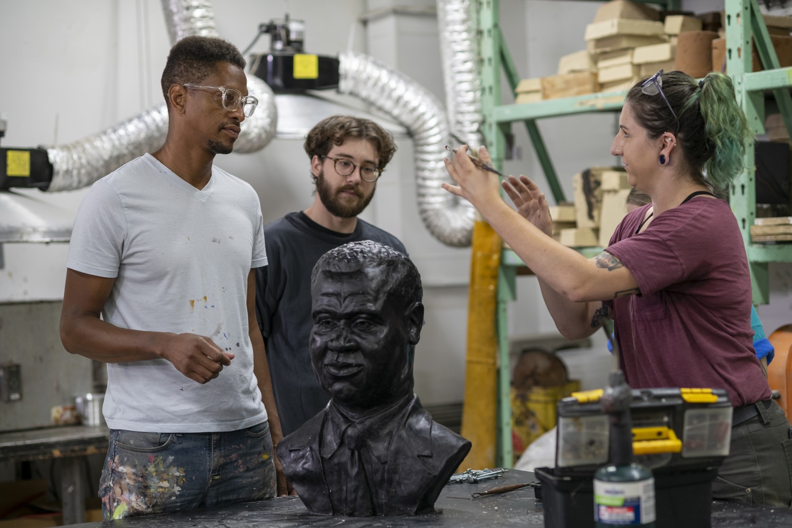 Three people stand near each other, next to an in-progress William Warfield sculpture.