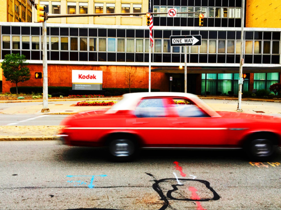A blurry car motors by the Kodak building.