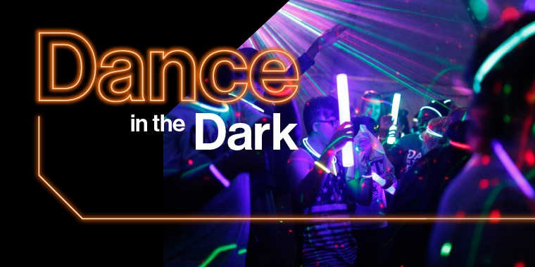 Students dancing in the dark with glow sticks and the words "Dance in the Dark" in neon text