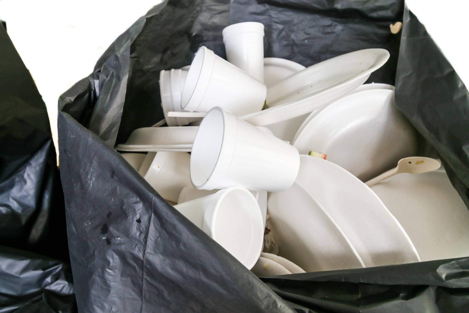 garbage  bag filled with disposable styrofoam cups and plates