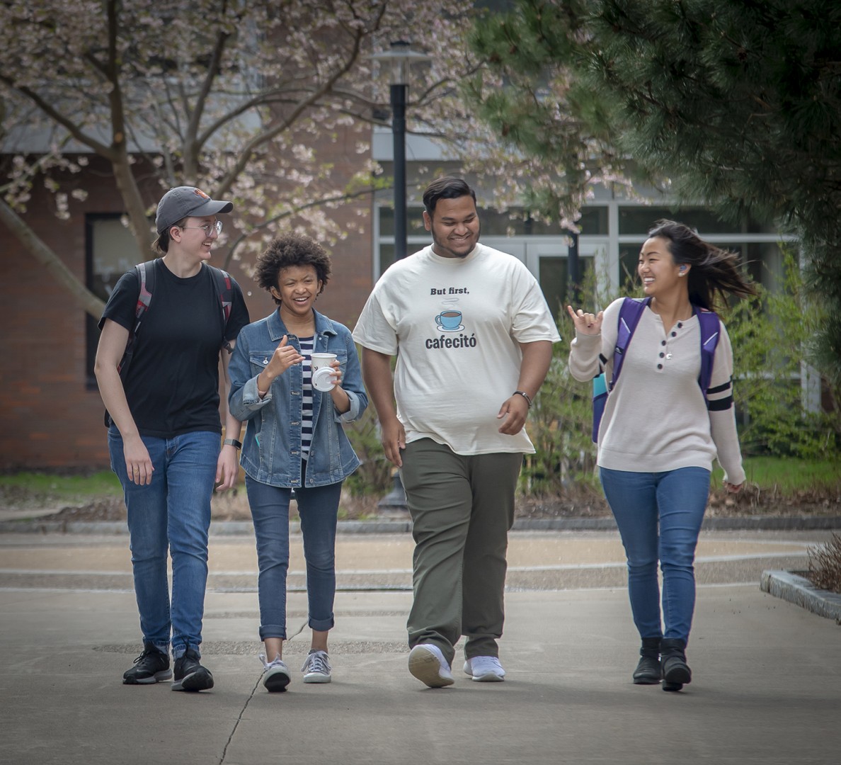 Four students walking on campus in single file.