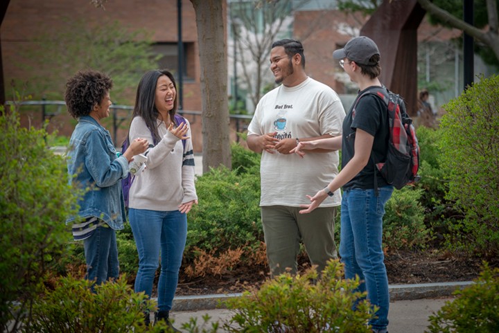 Four students standing in a semi circle on campus.