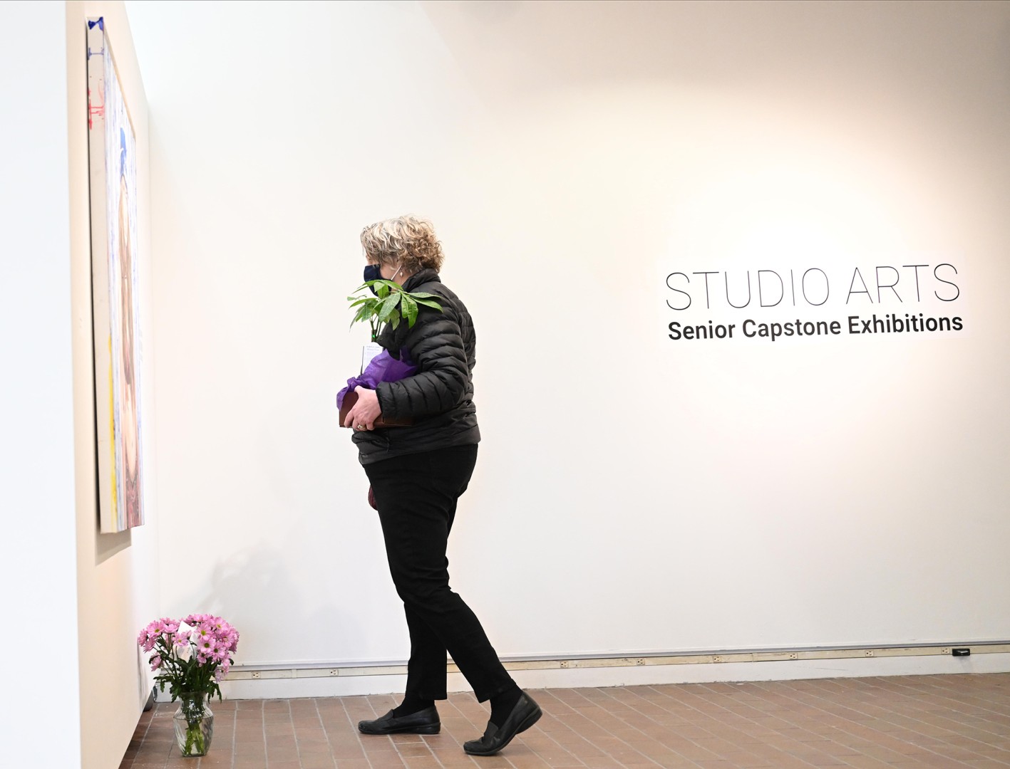 A gallery visitor looks at a painting mounted on the wall.
