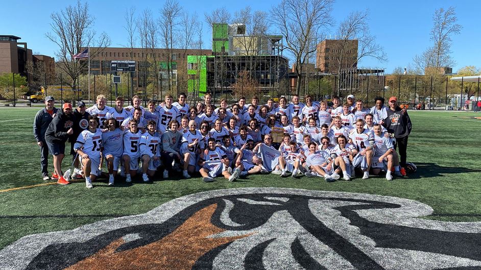 men’s lacrosse team and coaches in the middle of the turf field.