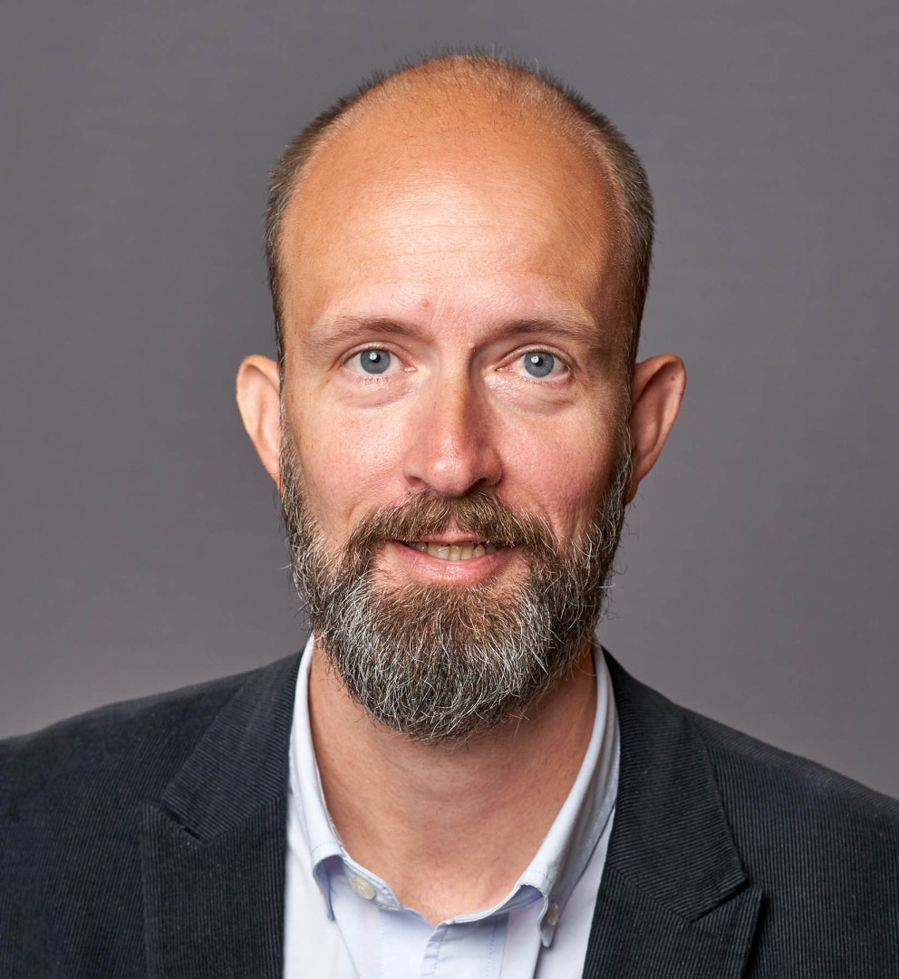 A bald gentleman wearing a dark jacket with a white shirt underneath