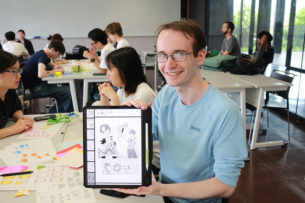 A student holds up a tablet with a manga illustration on it.