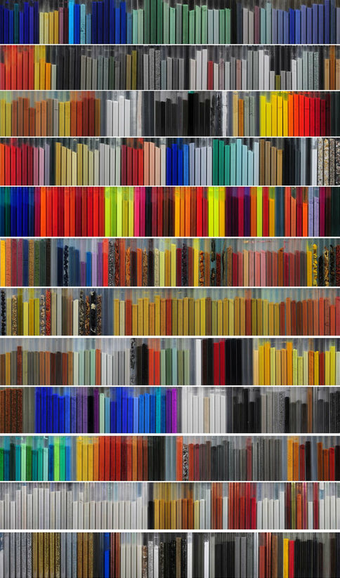 A large grid of pigment samples arranged in rows, each row displaying many rectangular swatches in a wide range of colors. The pigments include blues, greens, grays, blacks, yellows, oranges, reds, browns, metallics, and multicolored patterns. Some rows feature very bright, neon-like hues, while others contain muted earth tones or textured finishes. The overall effect is a dense, colorful catalog of pigment options.