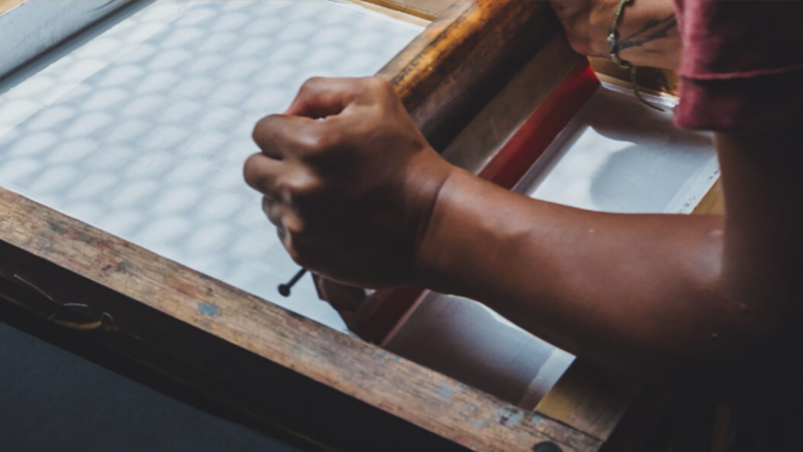 Close-up of hands using a brayer to apply ink on a textured surface, likely for printmaking.