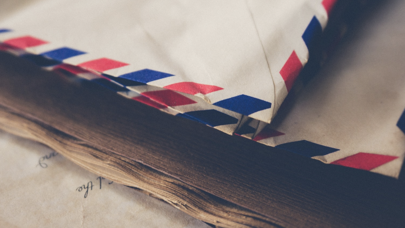 Close-up of a stack of envelopes with a red and blue striped border, resting on an aged piece of paper with text.