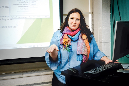 Woman stand behind computer and in front of projector screen.