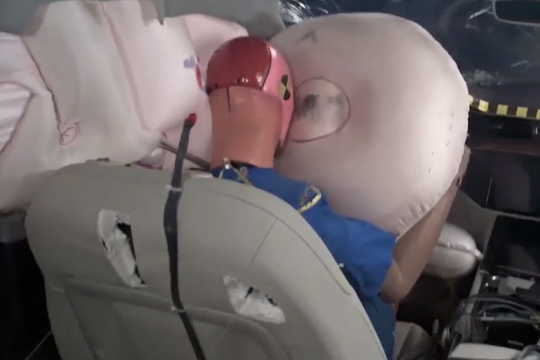 crash test dummy in driver's seat hitting deployed airbag.
