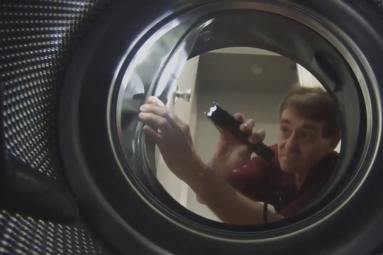 repairman looking at the inside of a washing machine with a flashlight.