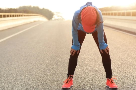 runner stopped in the middle of a road bent over with hands on their knees.