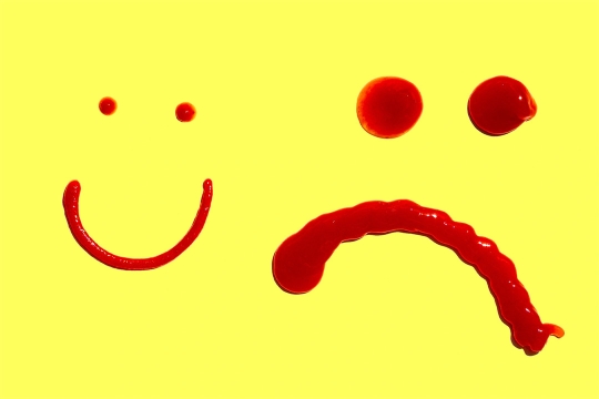 a smily face and a frown face made out of ketchup squirts.