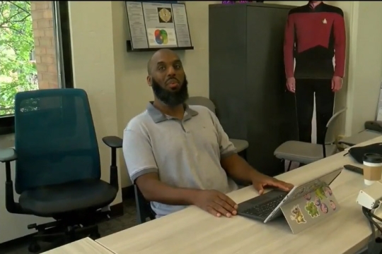 professor sitting a long table with a laptop computer.