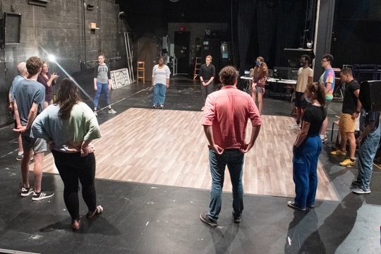 actors in a circle on stage doing a warm-up exercise.