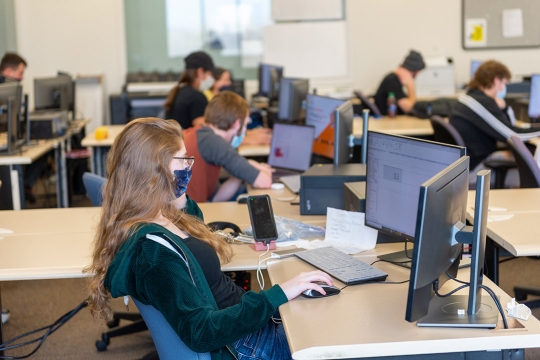 students wearing masks sitting at desks in a classroom.