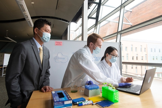 researchers looking at a laptop on a table with beakers and vials.