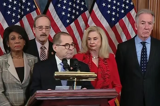 Five congress people stand in front of US flags and a podium. 