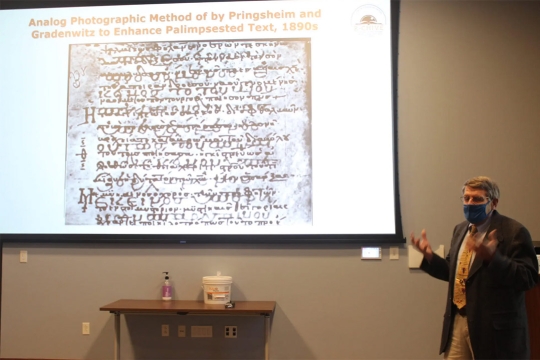 professor giving presentation with an ancient manuscript projected on a screen.