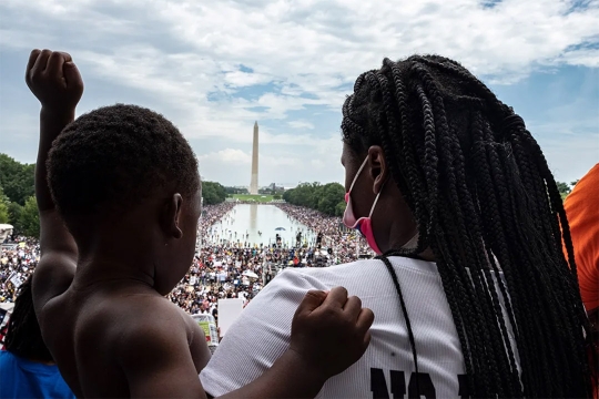 woman holding a child looking out at a crowd in front of the Washington Monument.