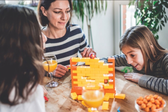 mother and two children playing a game with yellow and orange bricks.