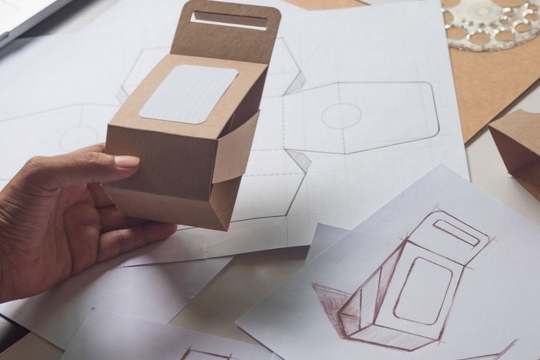 a cardboard box prototype next to a drawing of the box.