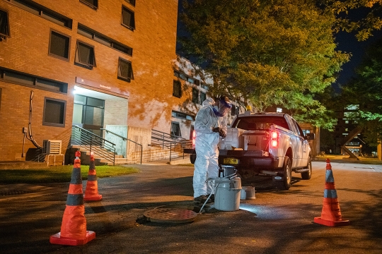 worker in a hazmat suit taking wastewater sample from a container in a manhole.